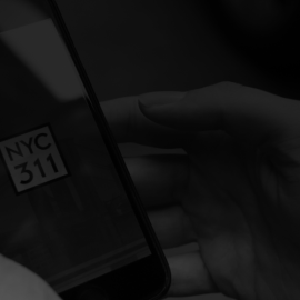Photo of hands holding a phone displaying the NYC311 logo